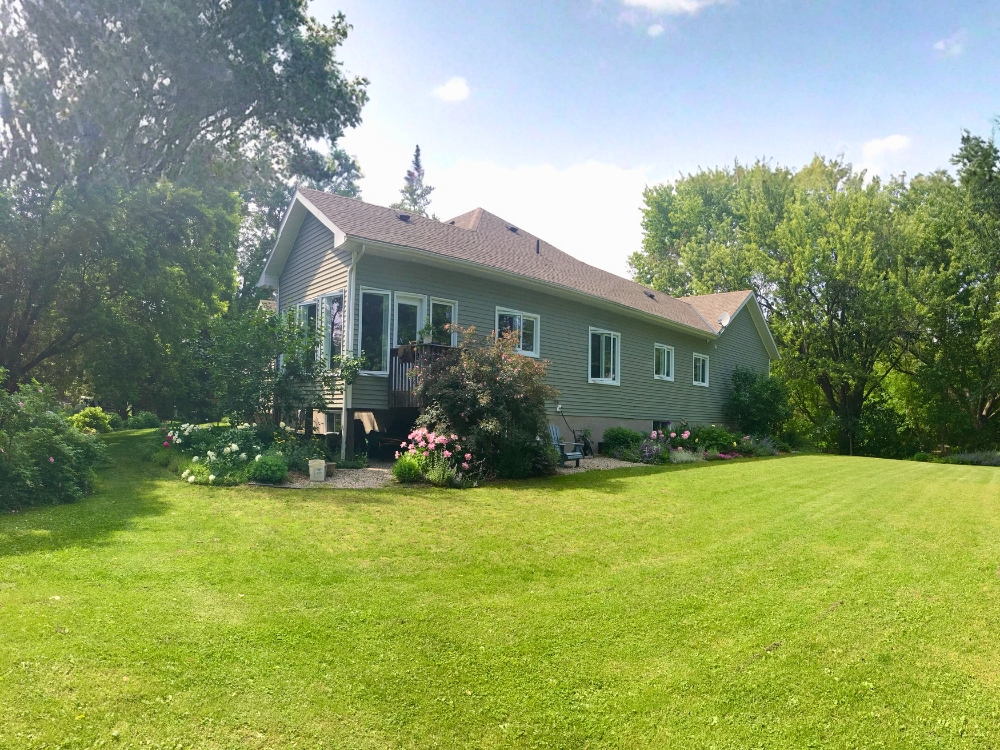 Rear exterior of 25 George Street, Westport Ontario, with mature gardens and lawn in summer